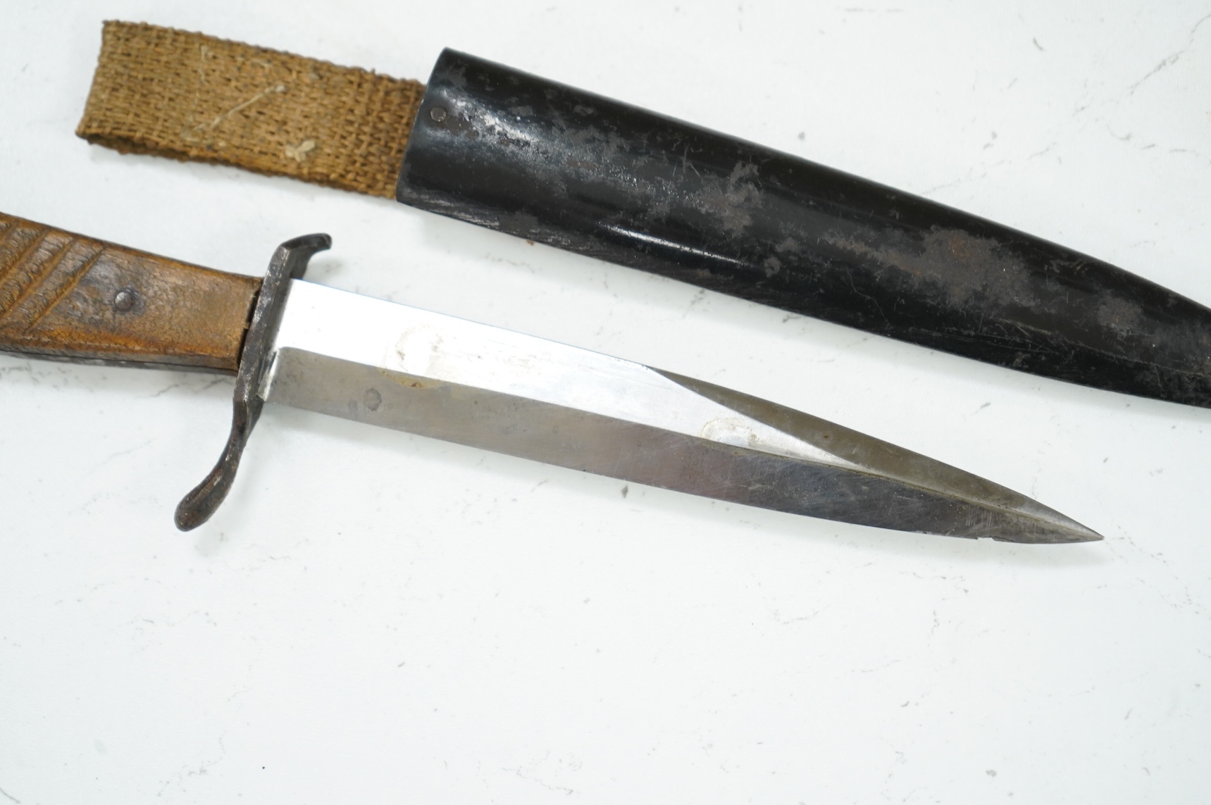 A First World War German Fighting Knife, with two piece wooden grip and steel cross guard, in original steel scabbard with canvas belt loop mount, single edged unmarked blade, blade 14cm, overall 25.5cm.